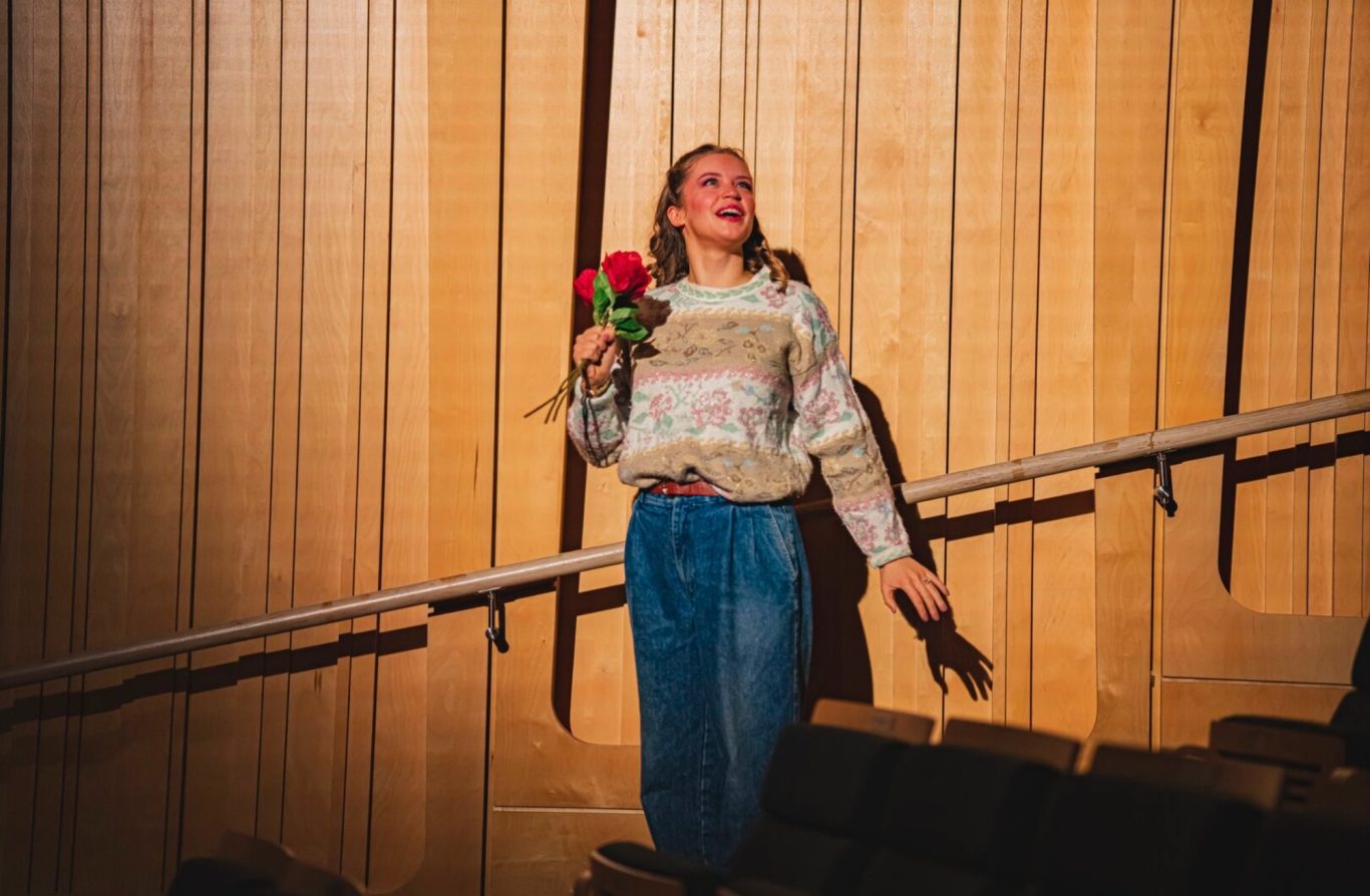 Eurydice, Orphée aux enfers A girl holding flowers descends down auditorium stairs, lit in a bright wash